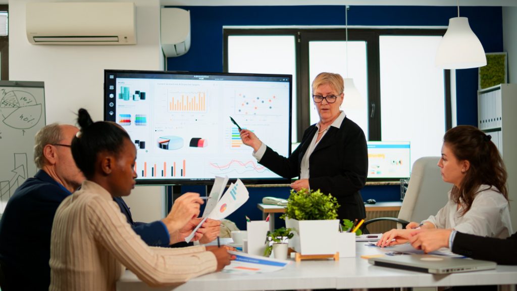A woman presents web development services in Dallas to an engaged audience of diverse individuals.