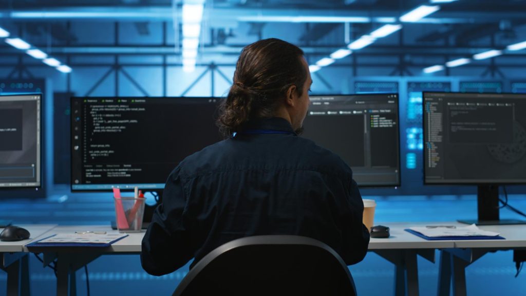 A man working at a desk with three computer screens, focused on frontend development Austin.